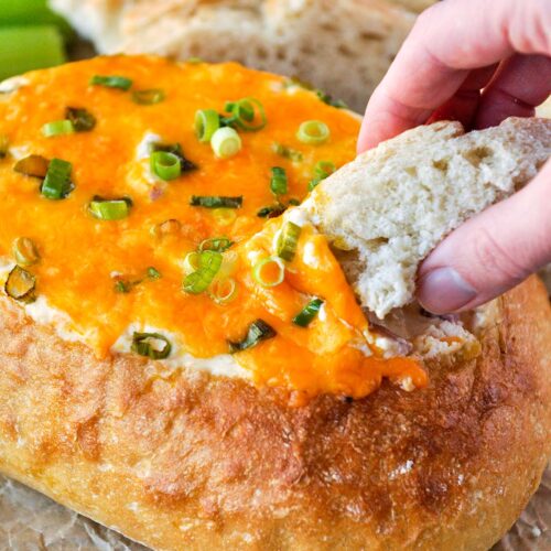 A piece of bread being dipped into a cheesy sin dip.
