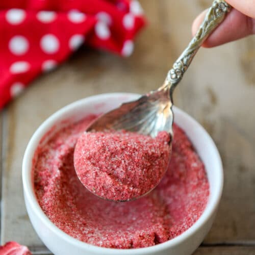 A spoonful of strawberry sugar over a small white bowl with a red and white polka dot towel.