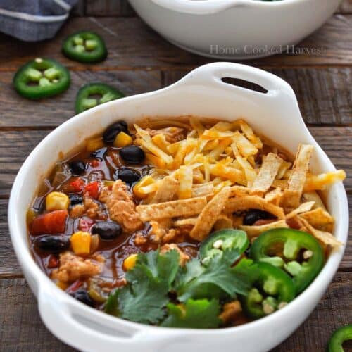 Two bowls of taco soup topped with cheese, jalapeños, and cilantro with a blue striped towel.