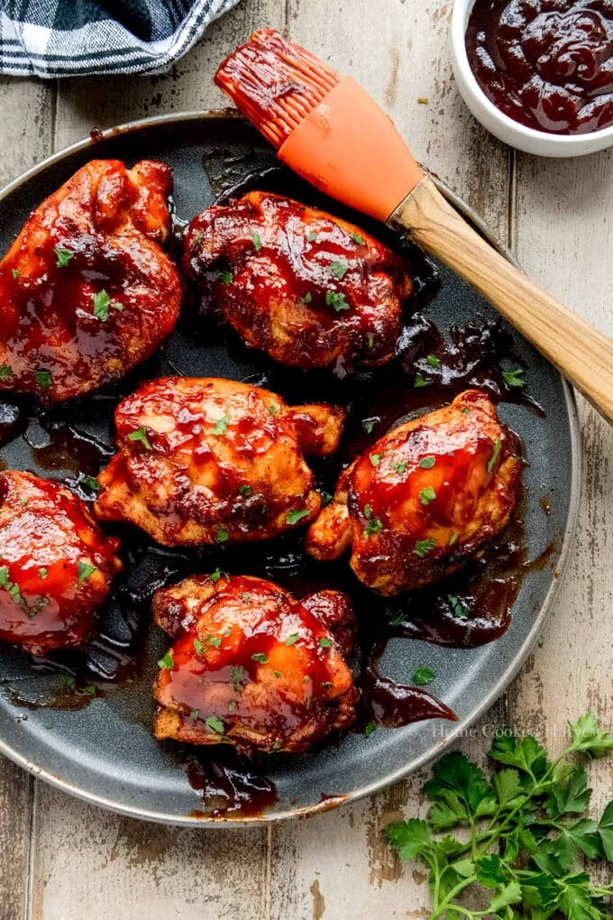 Above view of air fried barbecue chicken on a plate with a basting brush and a bowl of sauce.
