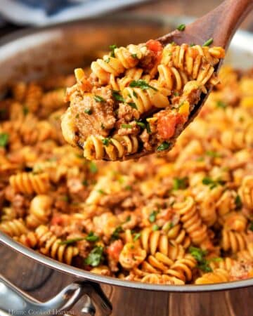 A spoonful of pasta above a pan full of pasta.