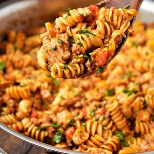 A spoonful of pasta above a pan full of pasta.