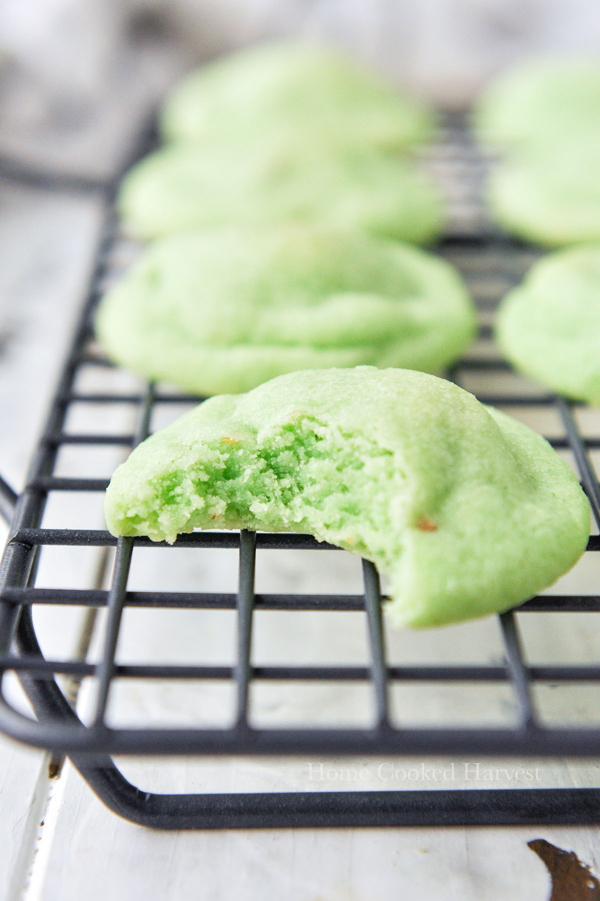 Pistachio cookies on a cooling rack, the front cookies is missing a bite.