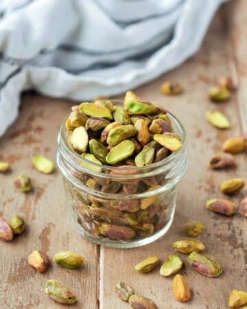 Roasted pistachios in a glass cup with pistachios around.