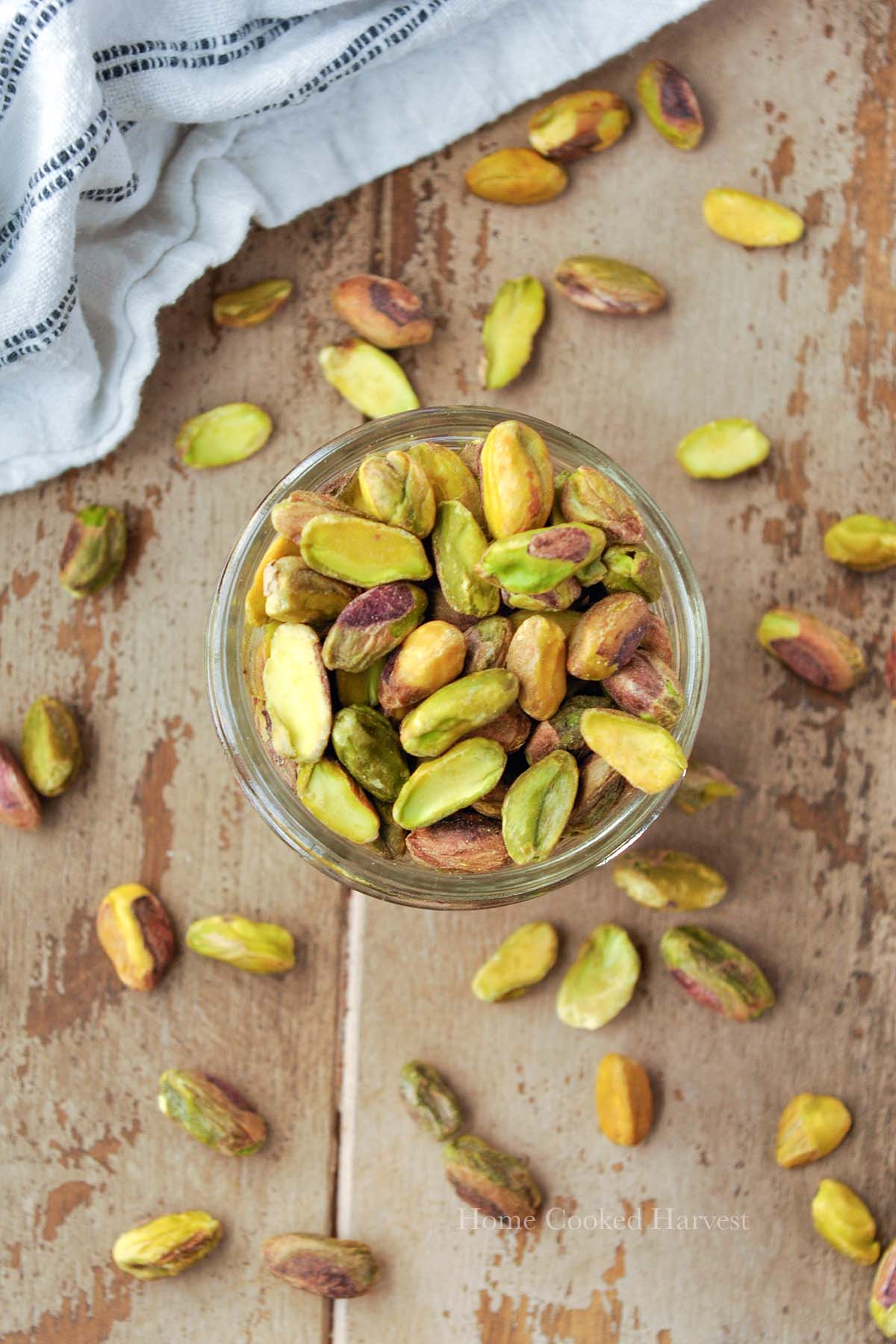 Roasted pistachios in a glass cup with pistachios around.