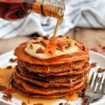 Syrup being poured over a large stack of carrot cake pancakes.