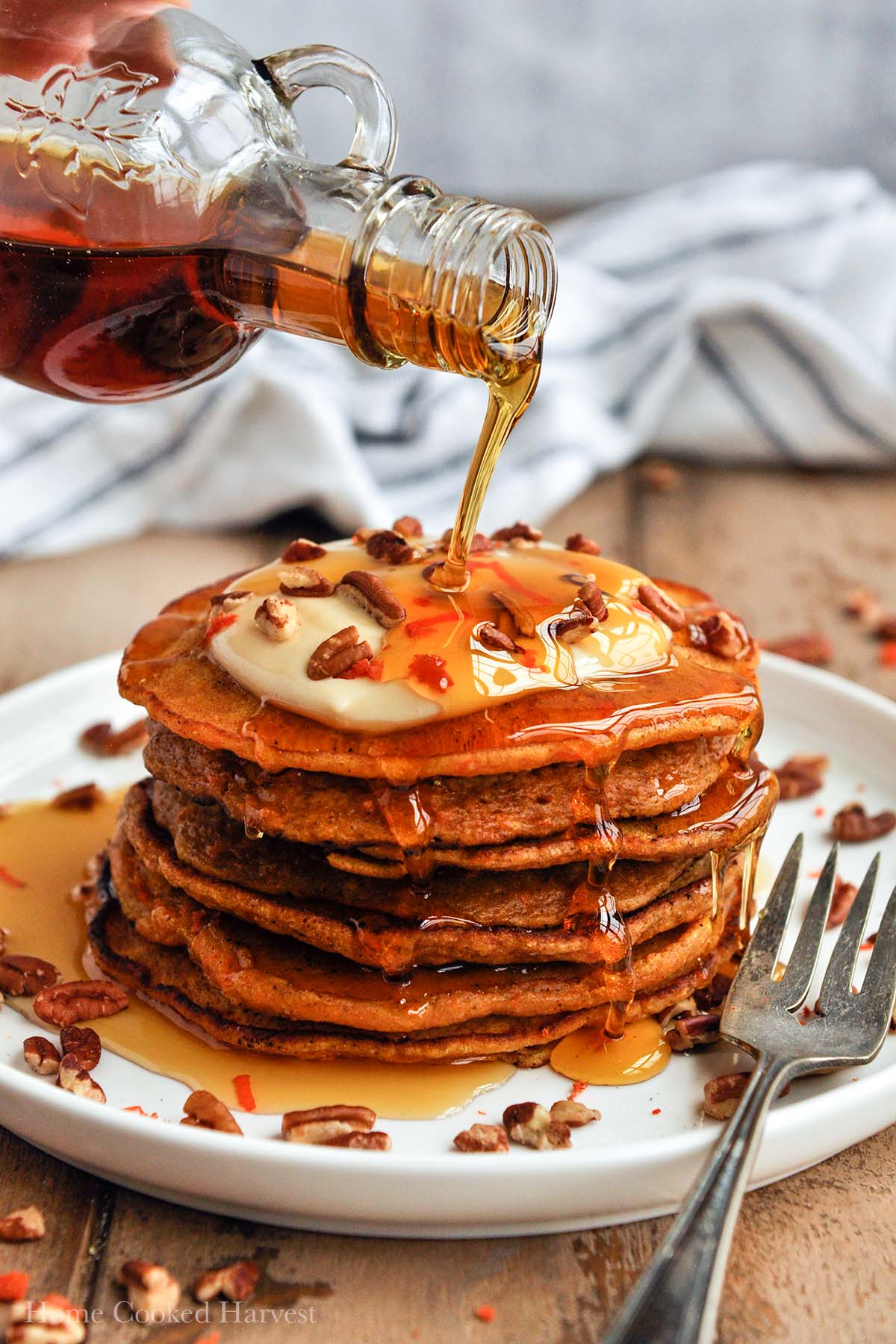 Syrup being poured over a large stack of carrot cake pancakes.