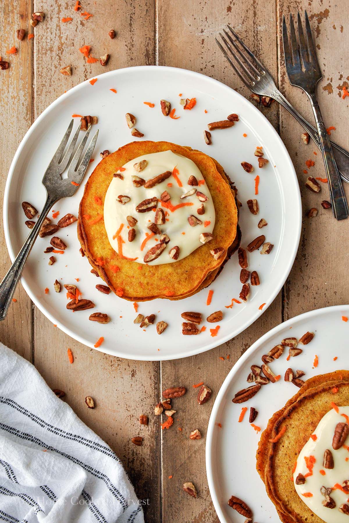 Above view of two plates of carrot cake pancakes topped with pecans, shredded carrots, and cream cheese topping.