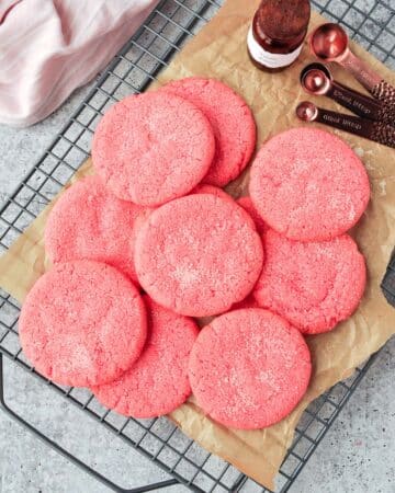 Above view of pink cookies on a cooling rack with a pink towel and measuring spoons.