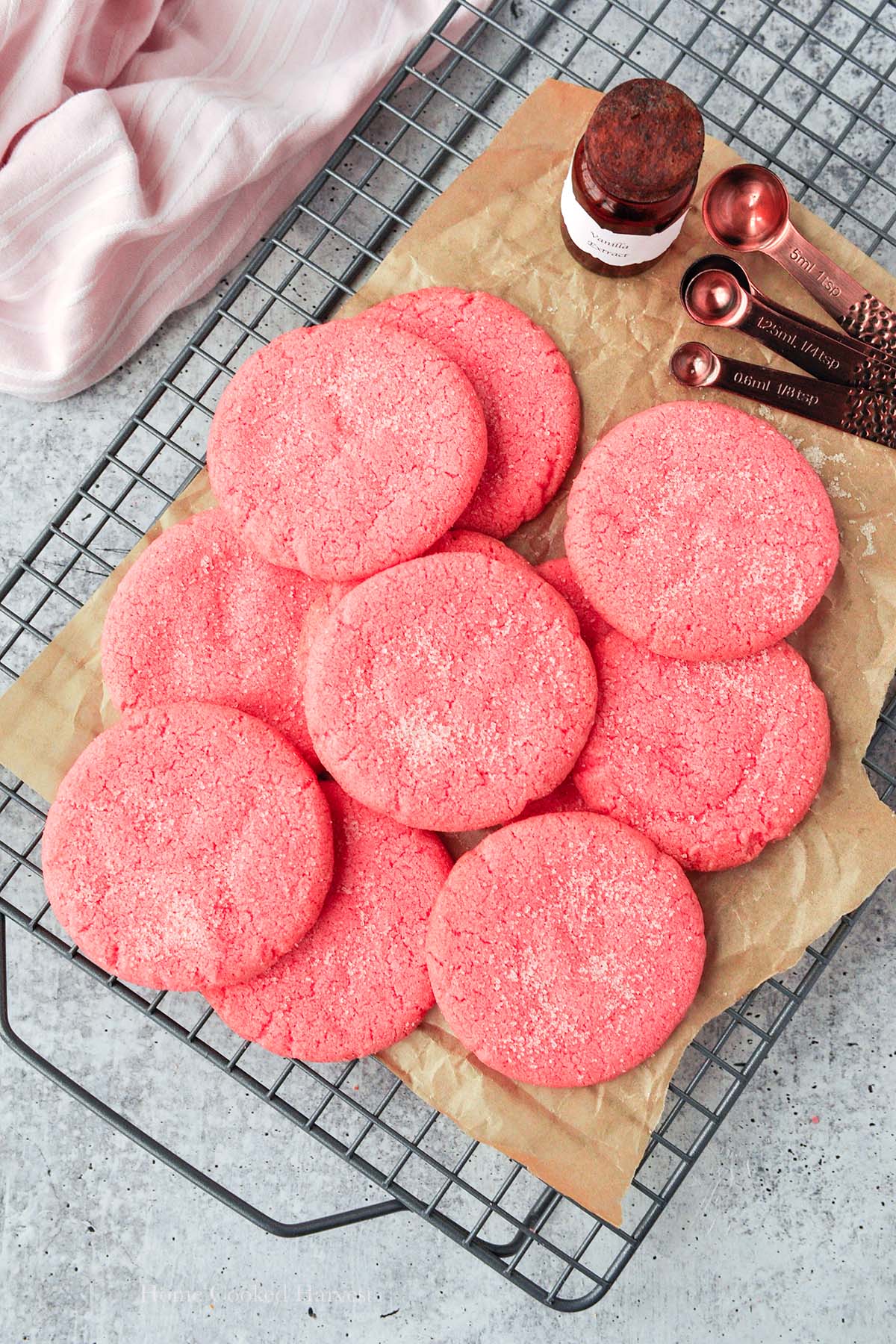 Above view of pink cookies on a cooling rack with a pink towel and measuring spoons.