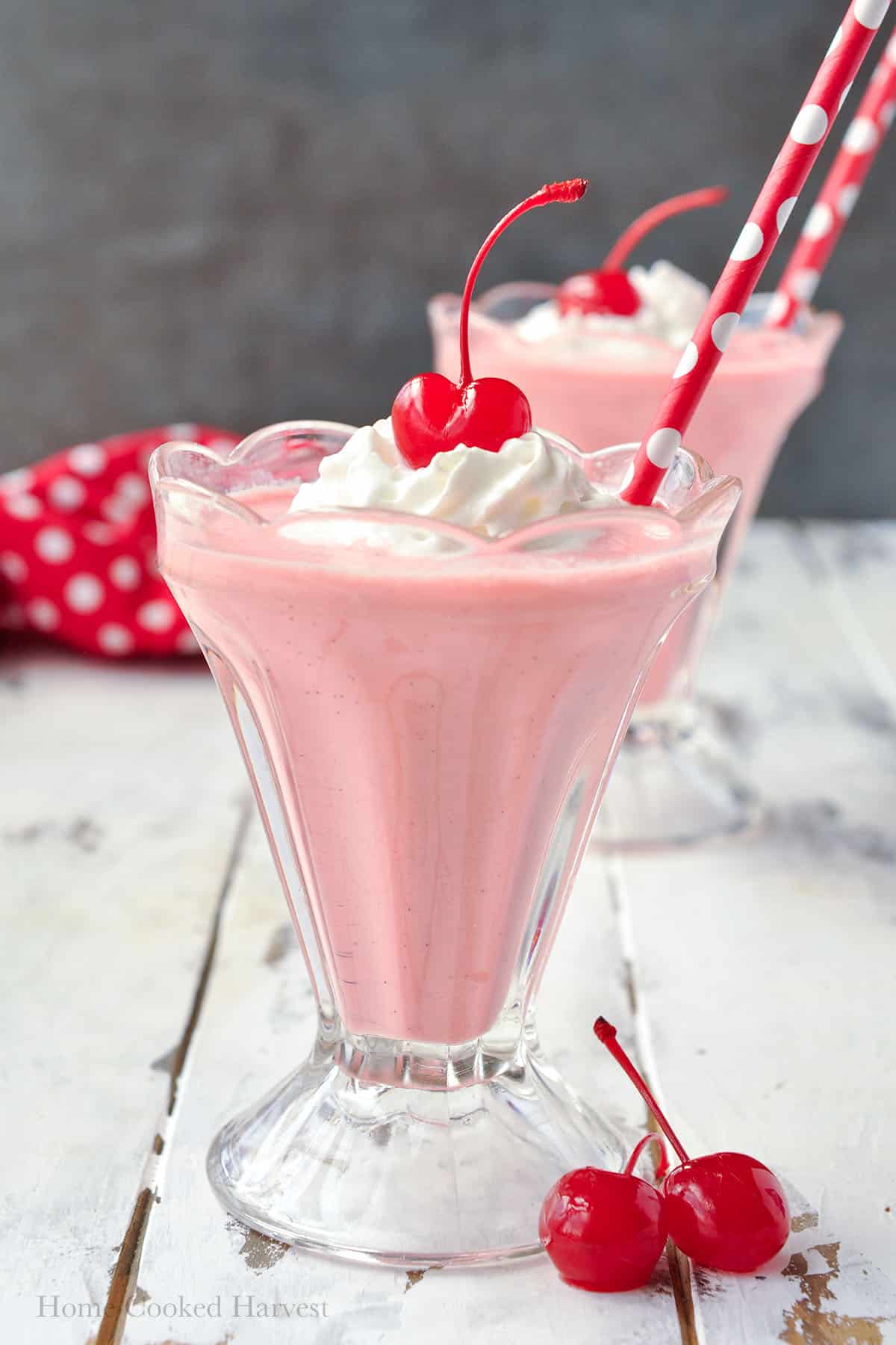 Up close of the pink squirrel cocktail topped with whipped cream, a cherry and a polka dot straw.