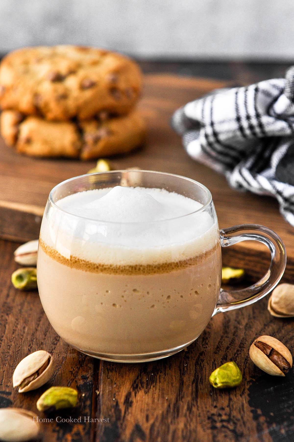 A closeup of a mug of a Starbucks pistachio latte with cookies in the background and pistachios around.