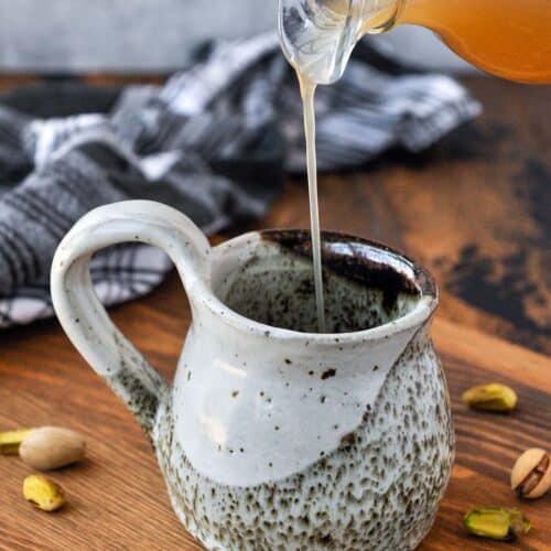 Pistachio syrup being poured into a coffee drink.