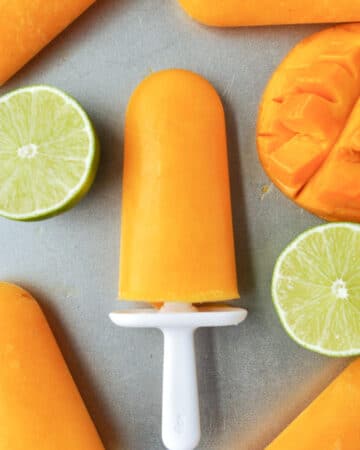 Mango ice popsicles on a tray with lime halves.