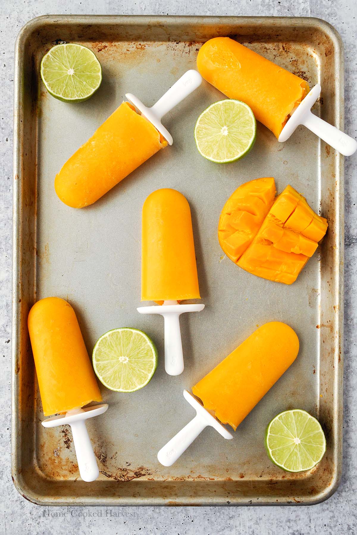 A tray with mango popsicles, lime halves, and half of a mango.