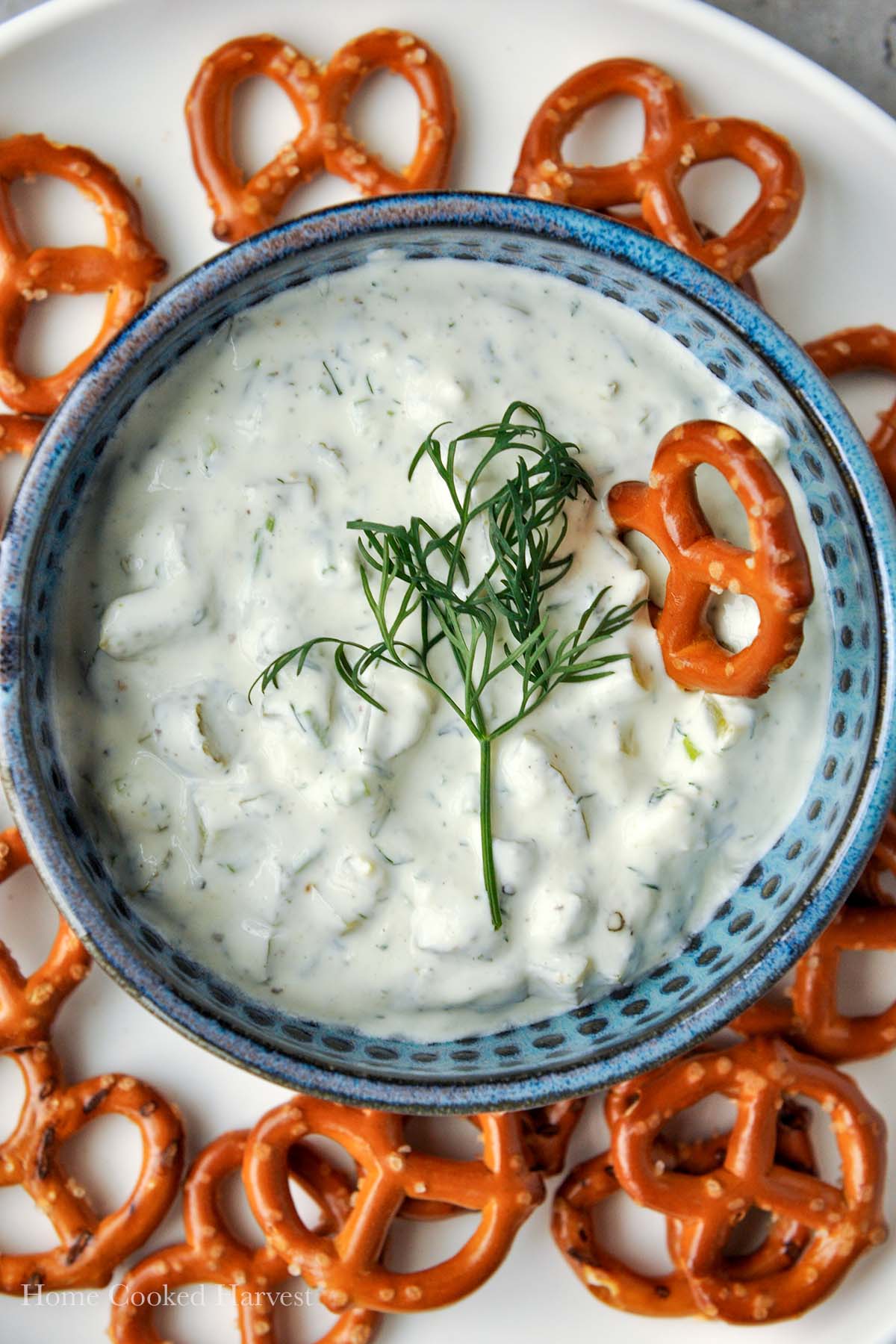 A close up of dill pickle dip with a pretzel in it and a sprig of dill.