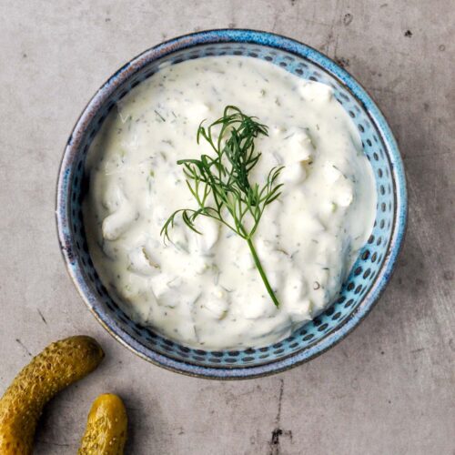 A blue bowel of pickle dip with a sprig of fresh dill and two pickles.