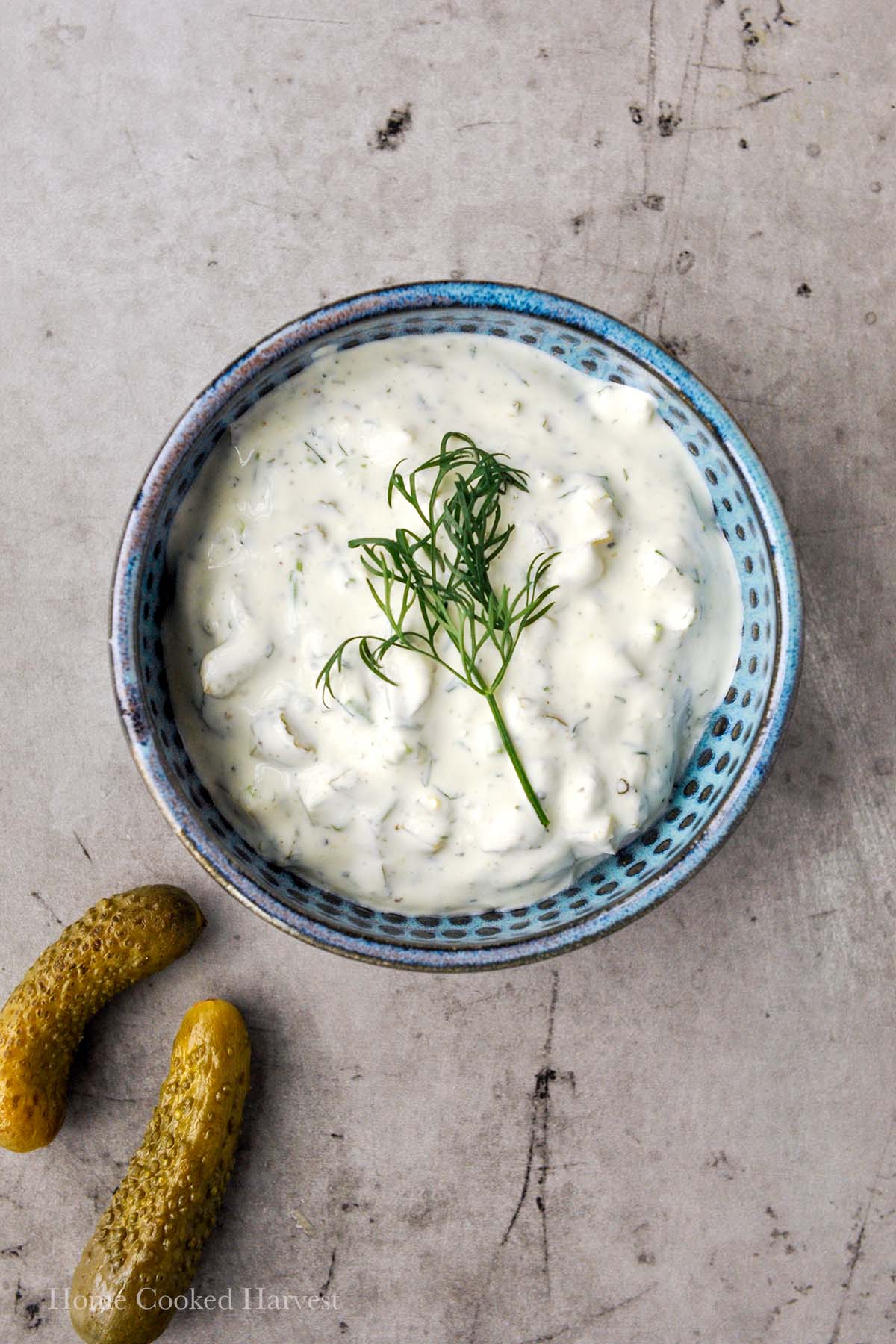 A blue bowel of pickle dip with a sprig of fresh dill and two pickles.