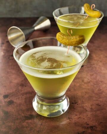 Two glasses of pickle juice martinis with a pickle garnish.