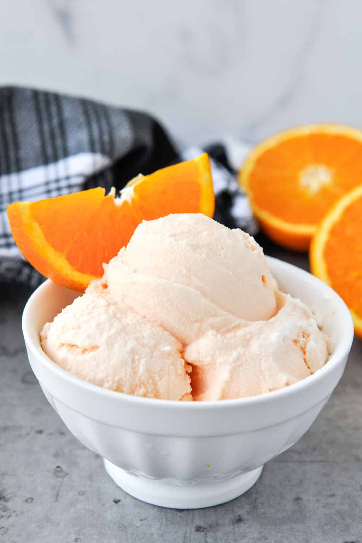 A bowl of ice cream with oranges in the background. Spoon in the foreground.