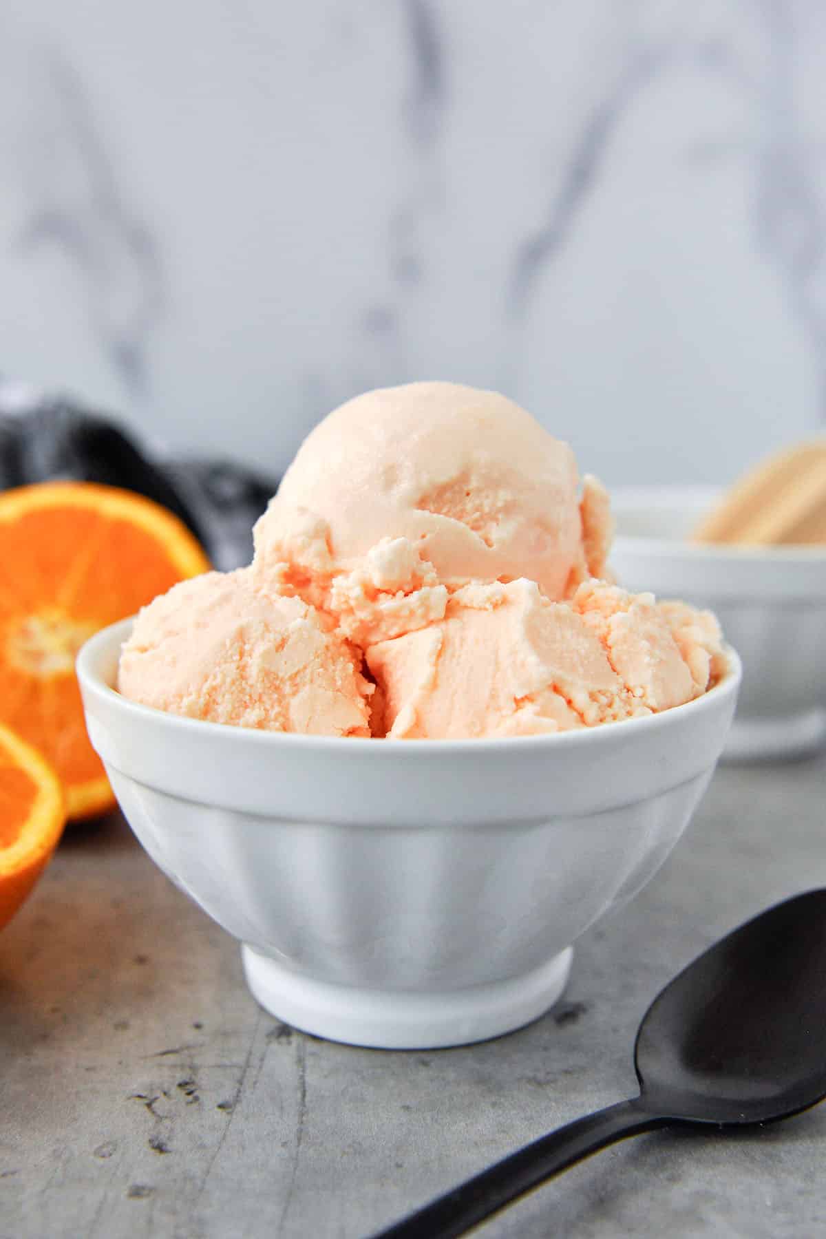 A bowl of ice cream with oranges in the background. Spoon in the foreground.