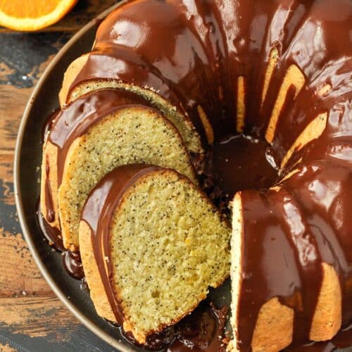 Above view of orange cake with some slices on a serving plate with an orange slice and a striped towel.