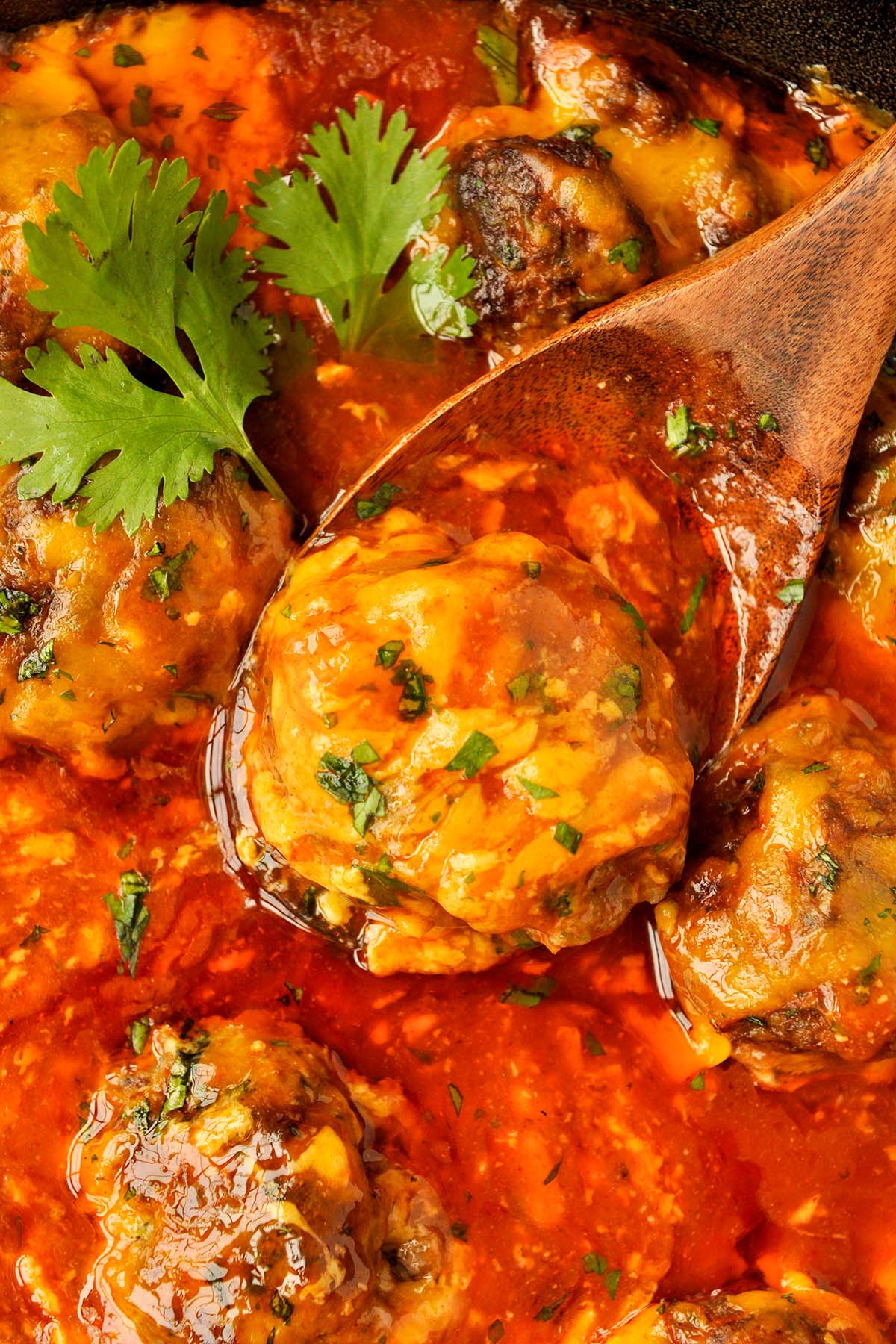 Up close of a pan full of saucy meatballs and on on a wooden spoon.