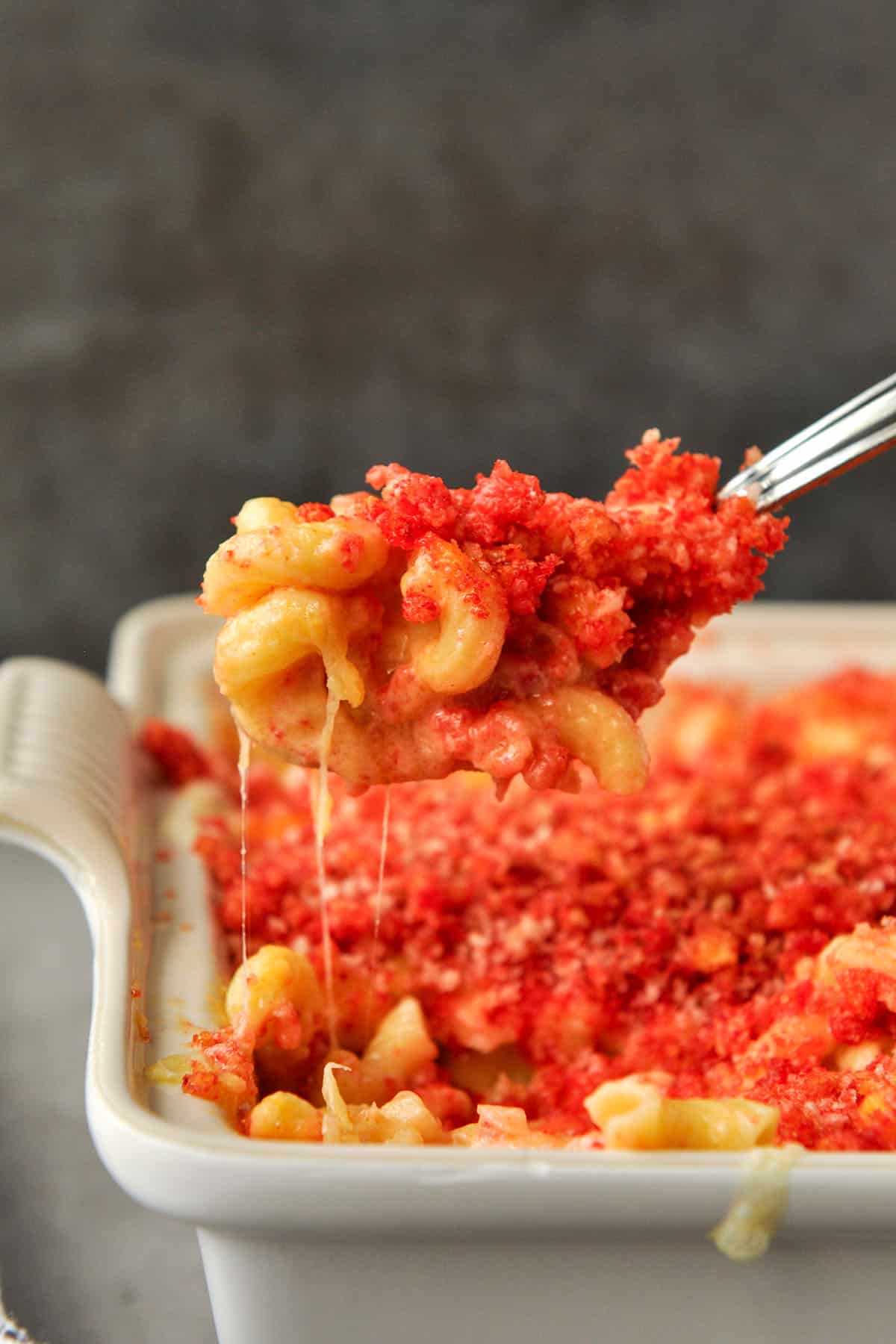 A spoonful of Cheeto macaroni and cheese over a baking dish.