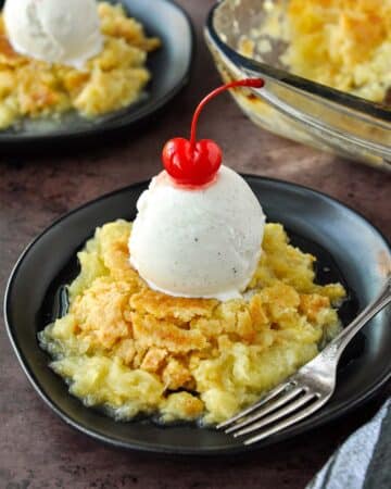 A plate of juicy pineapple dump cake topped with ice cream and a cherry.