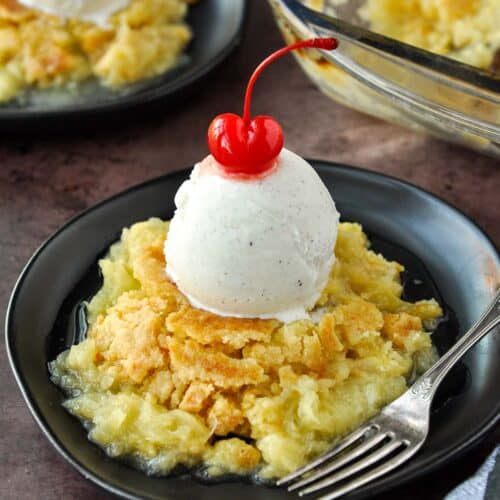 A plate of juicy pineapple dump cake topped with ice cream and a cherry.