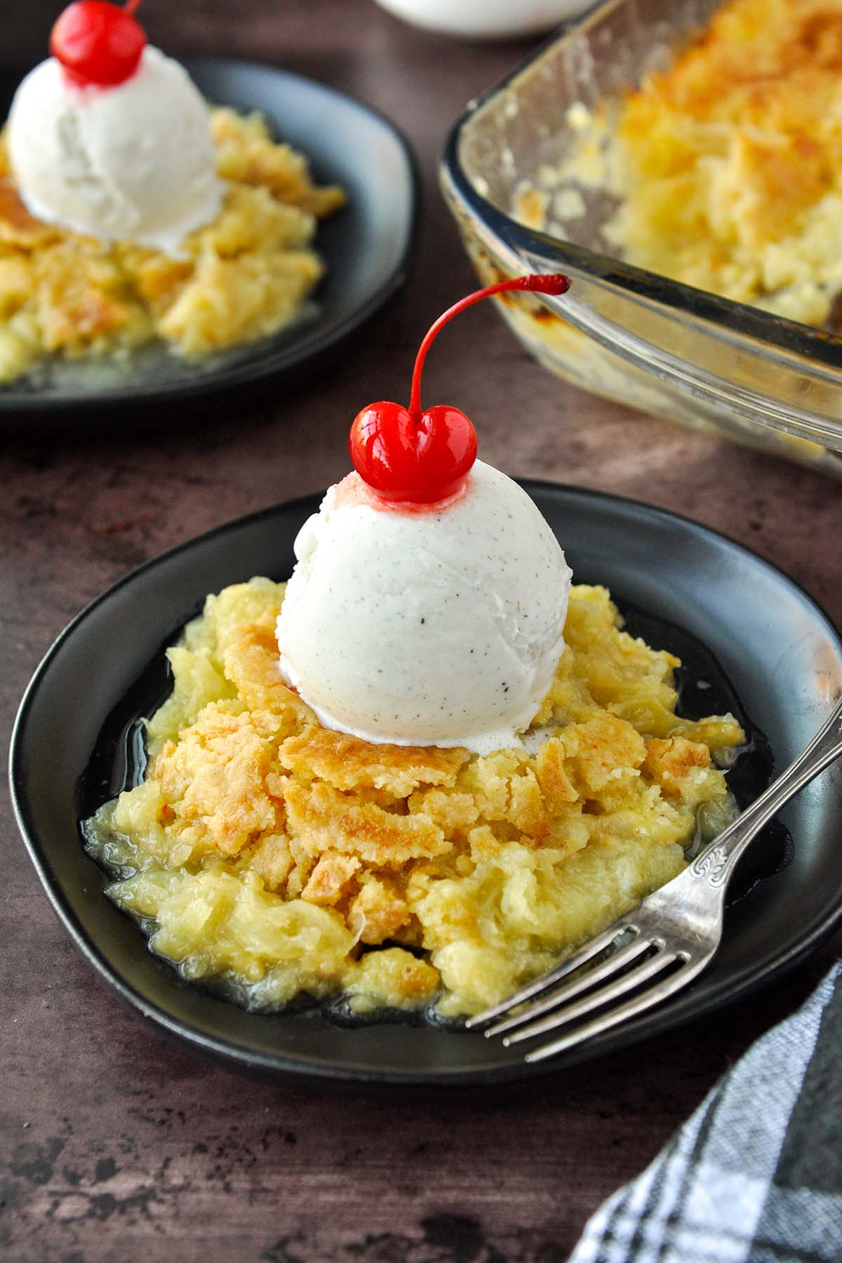 A plate of juicy pineapple dump cake topped with ice cream and a cherry.