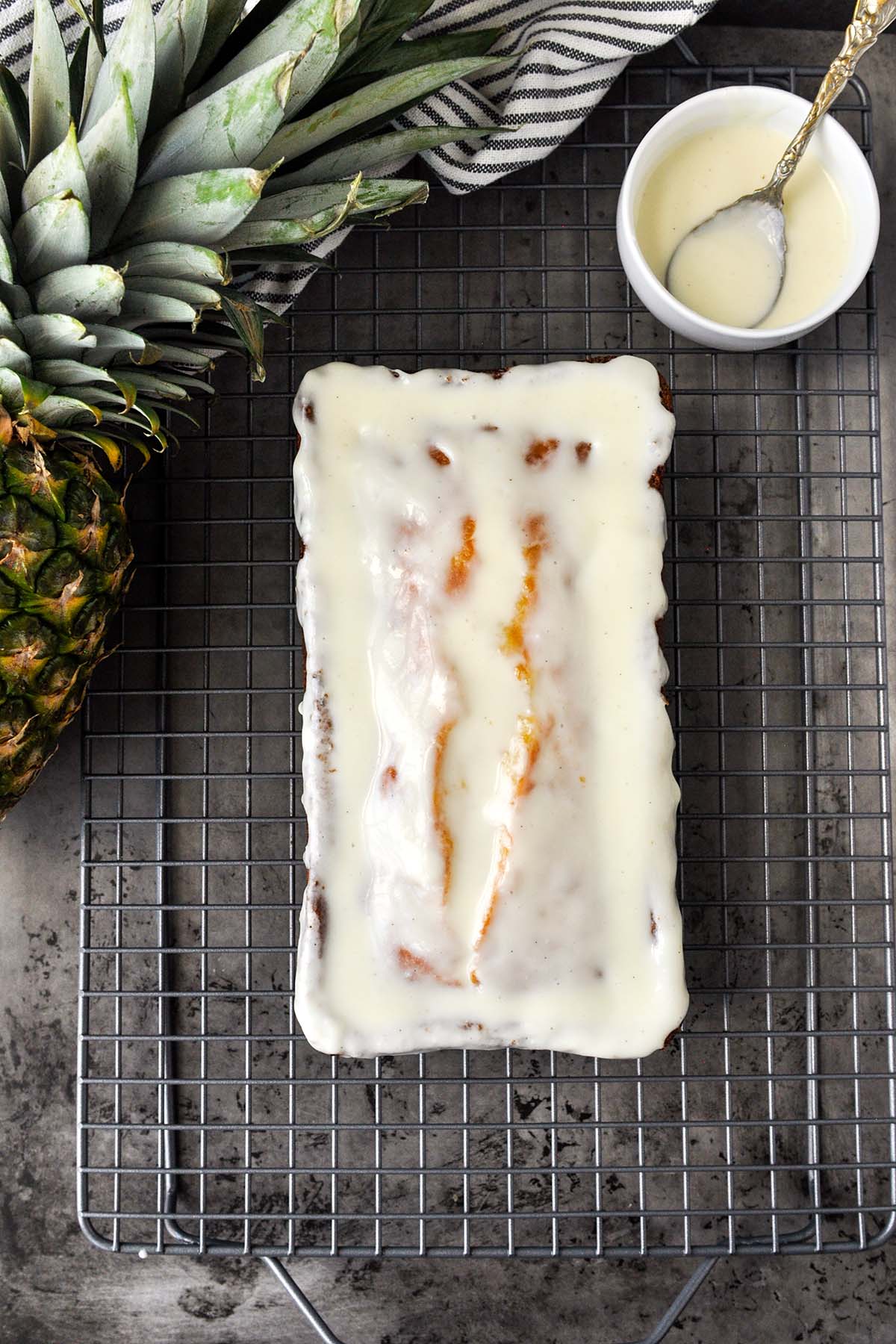 An above view of a glazed pineapple pound cake on a cooking rack with a pineapple.