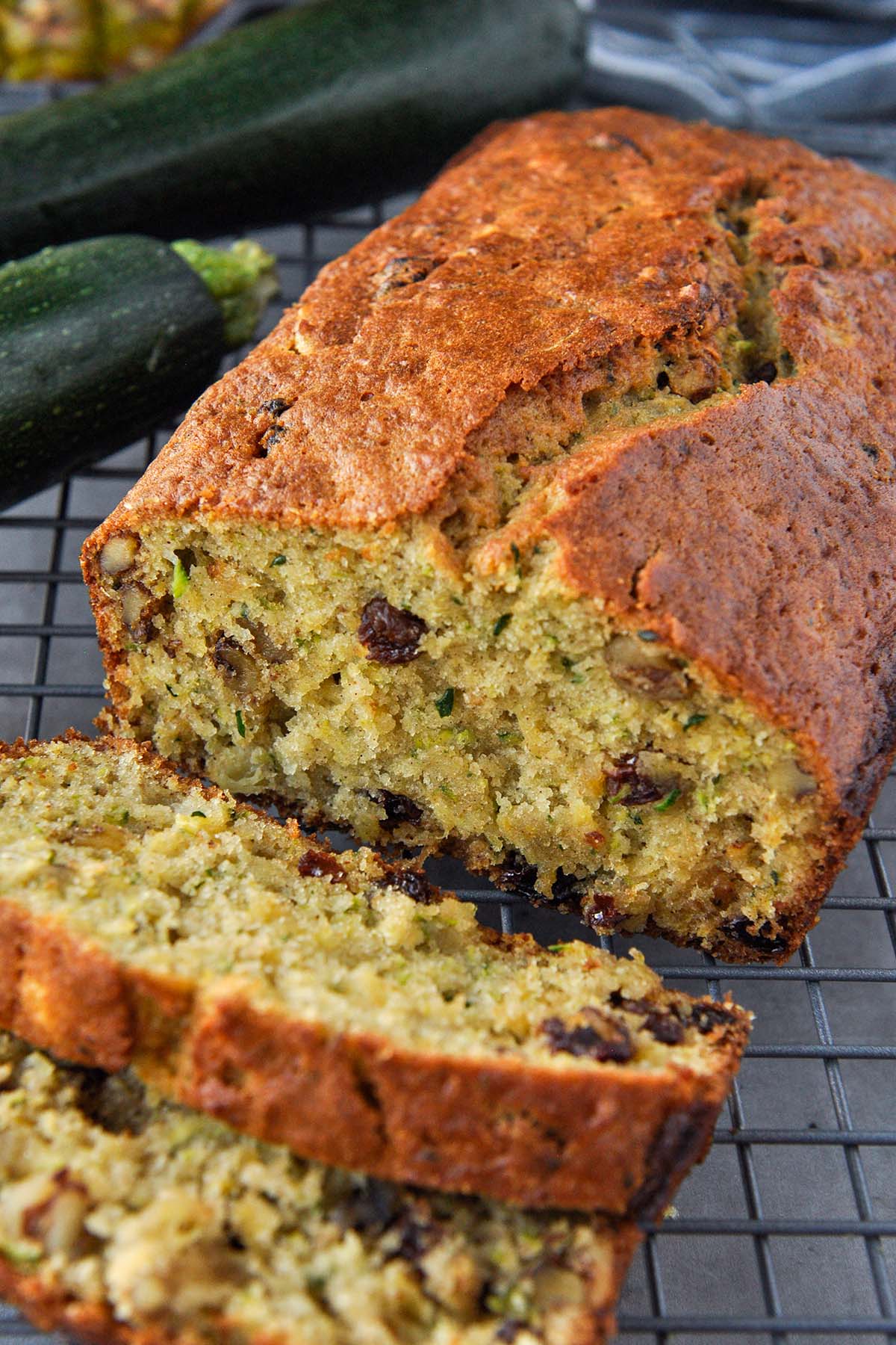 A loaf of pineapple zucchini bread with some slices cut and zucchini in the background.