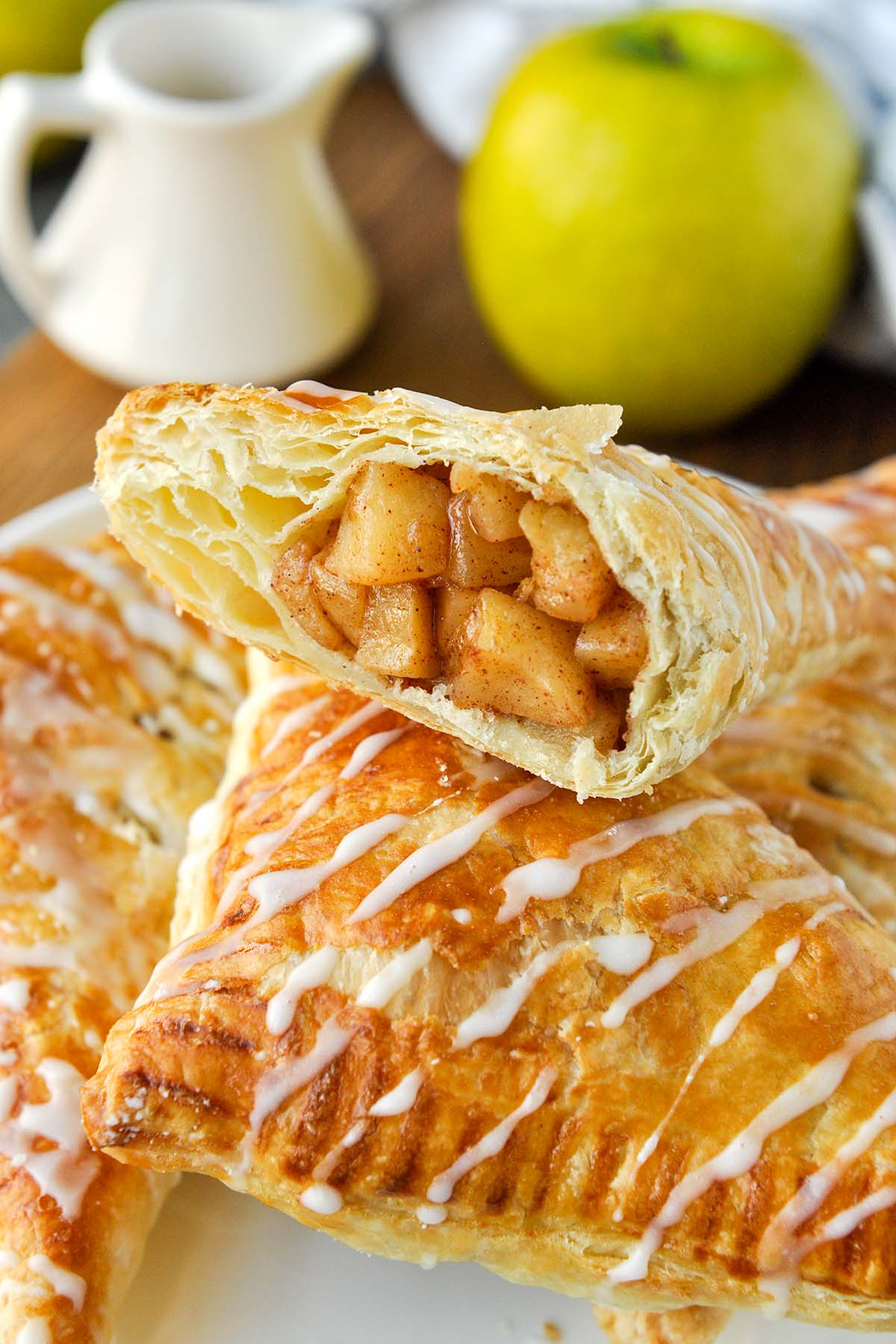 Half of an apple puff pastry on top of other pastries with an apple in the background.