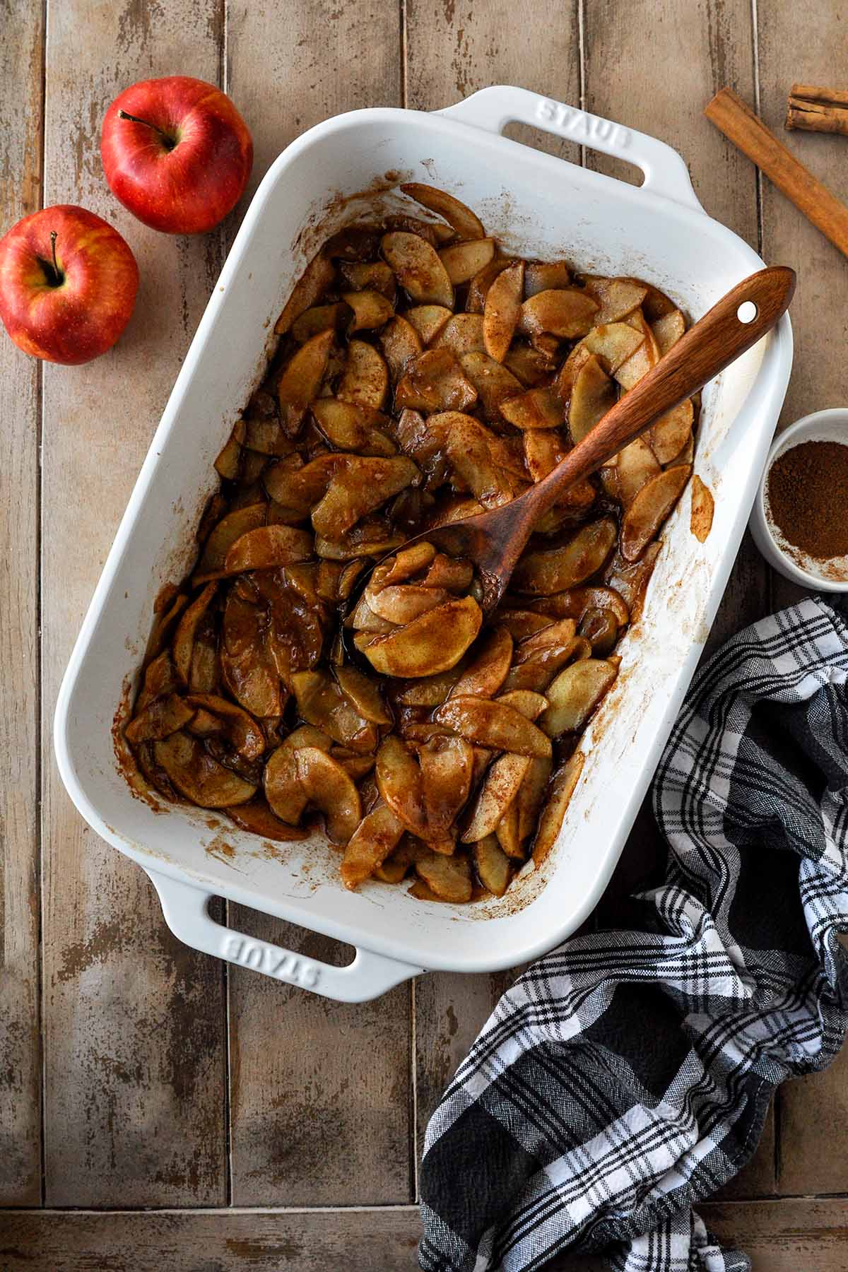 Above view of baking dish of apples with a black and white striped towel and whole apples.