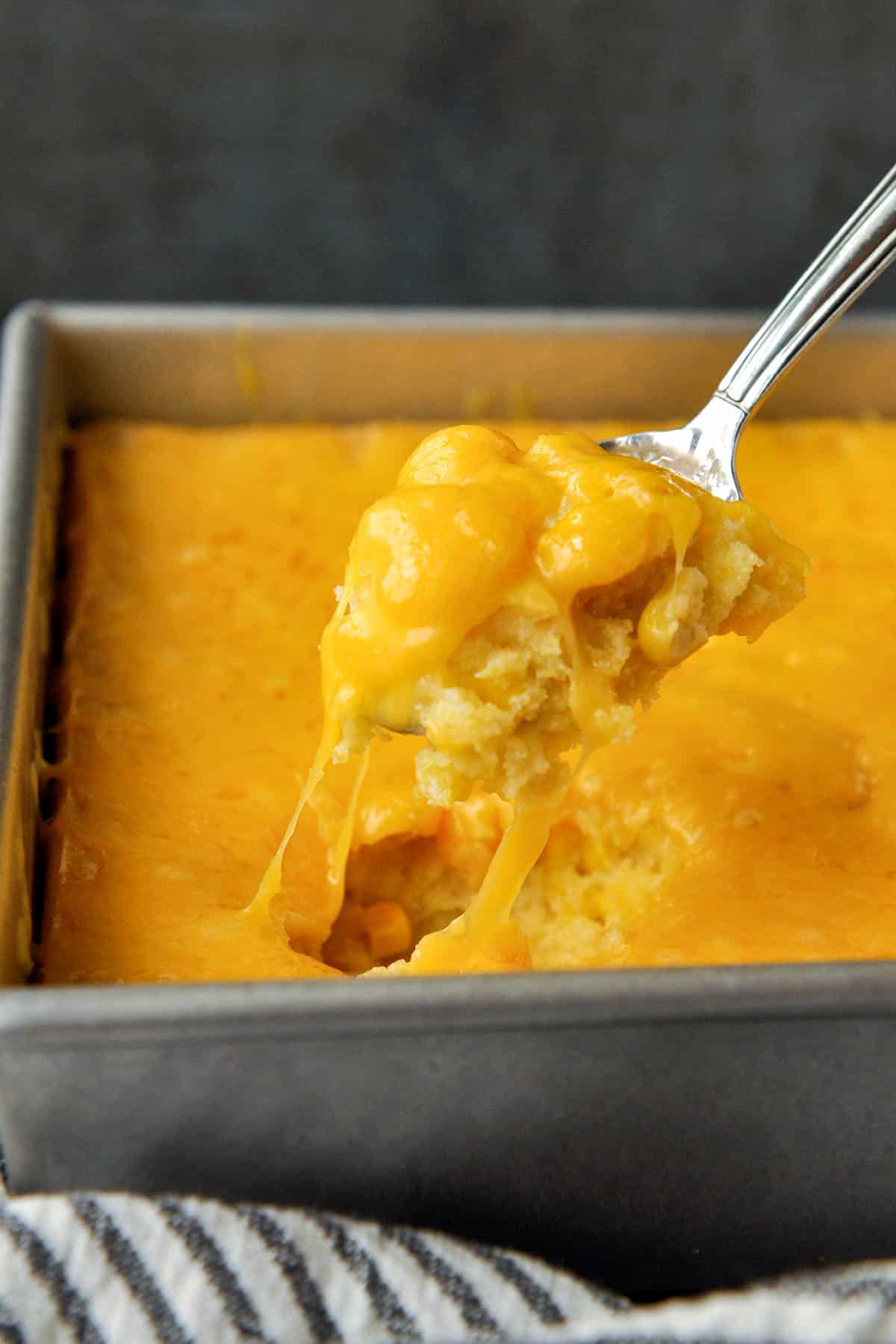 A large spoon full of baked corn casserole with gooey strings of cheese.