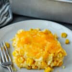 Corn casserole on a plate with a fork and the baking dish in the background.