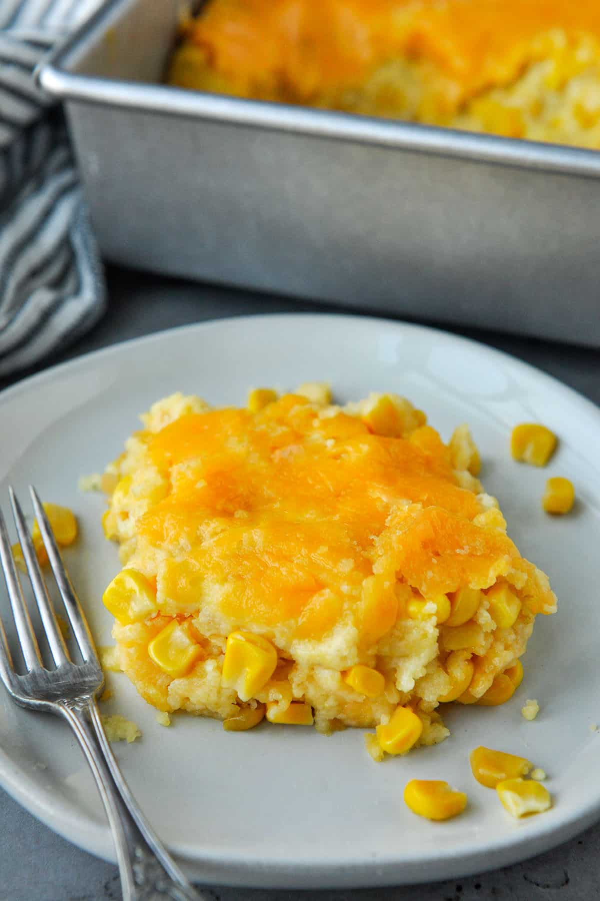 Corn casserole on a plate with a fork and the baking dish in the background.