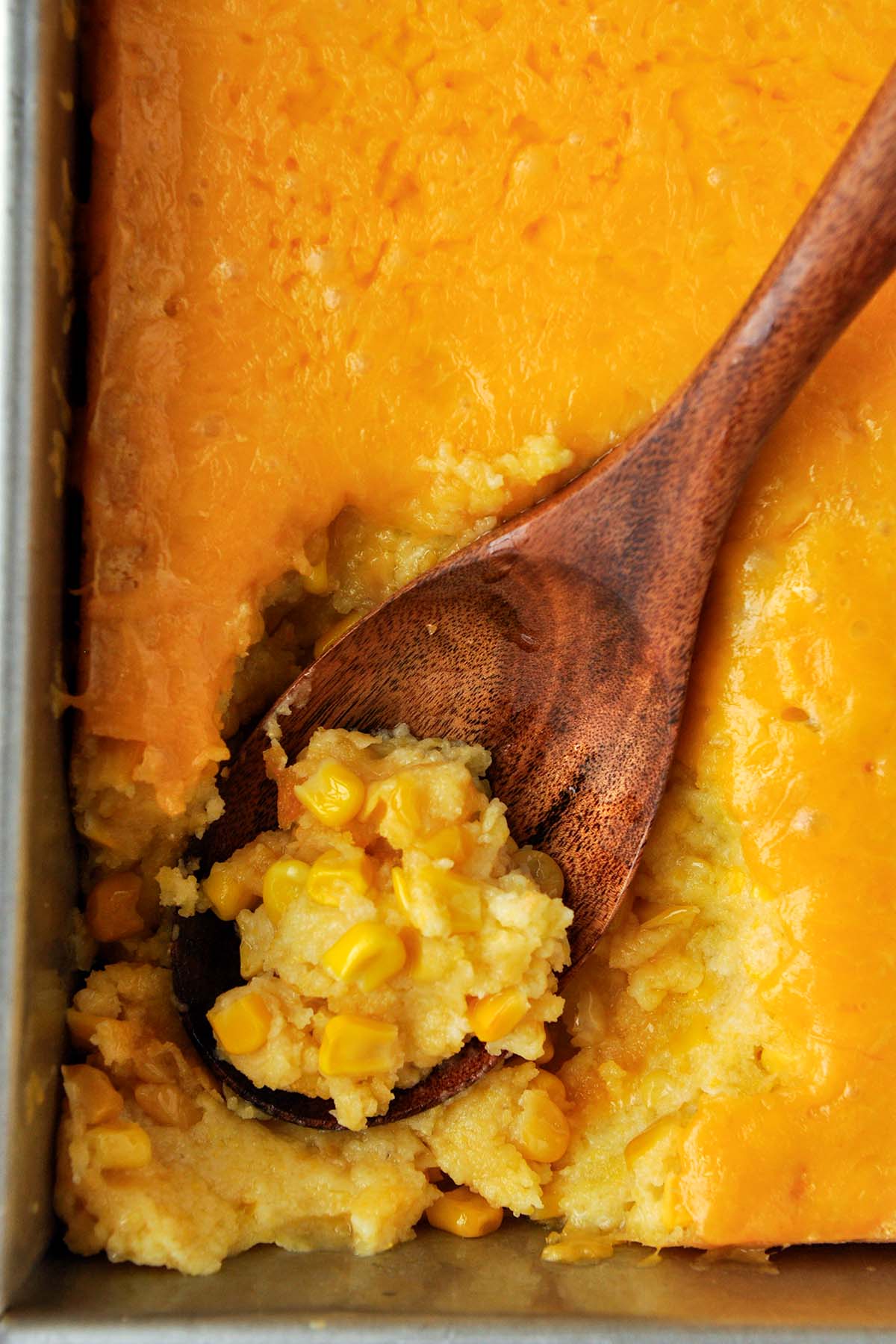 Above view of a pan of Paula's corn casserole with a wooden spoon.