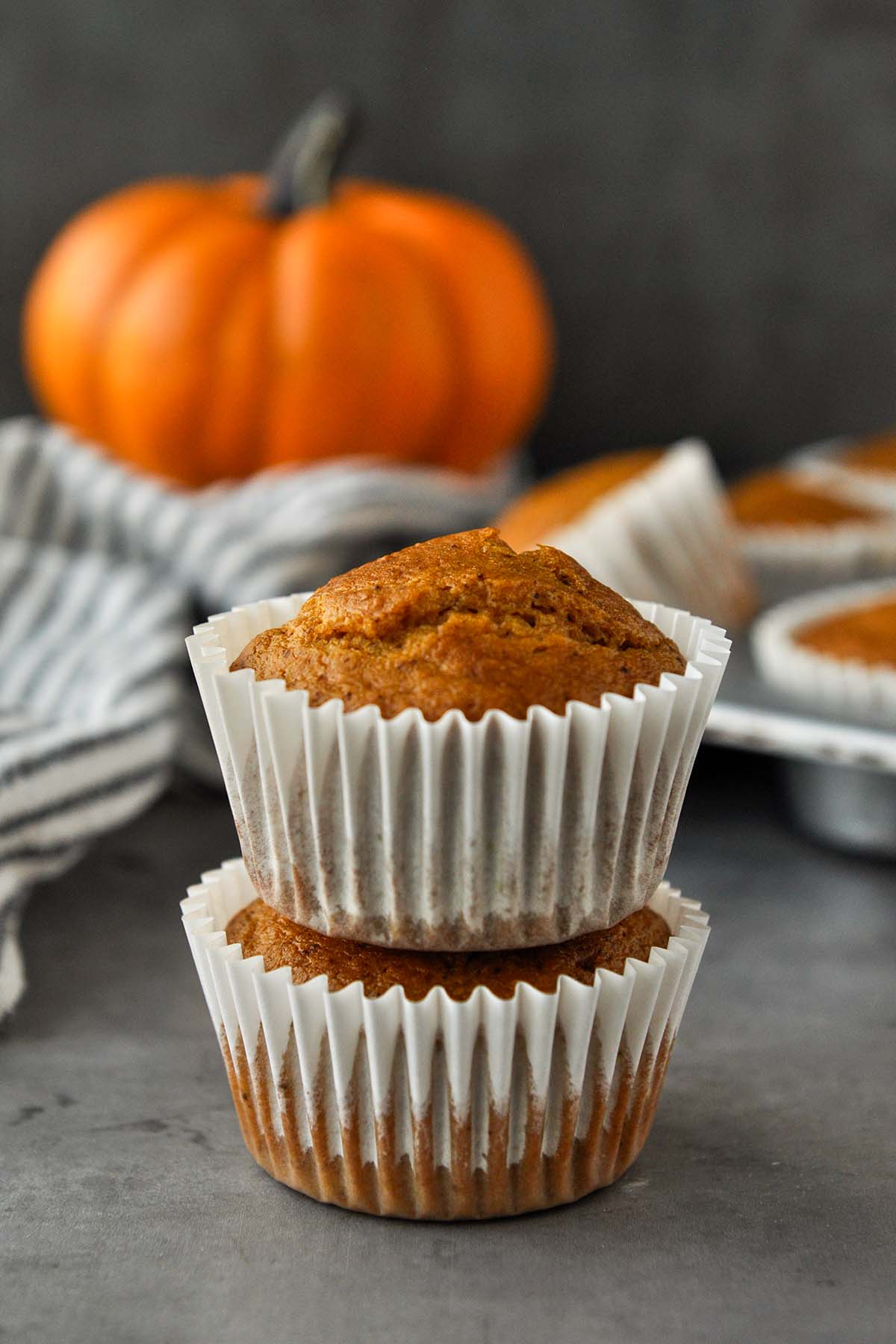 Two muffins stacked on top of each other with muffins and pumpkin in the background.