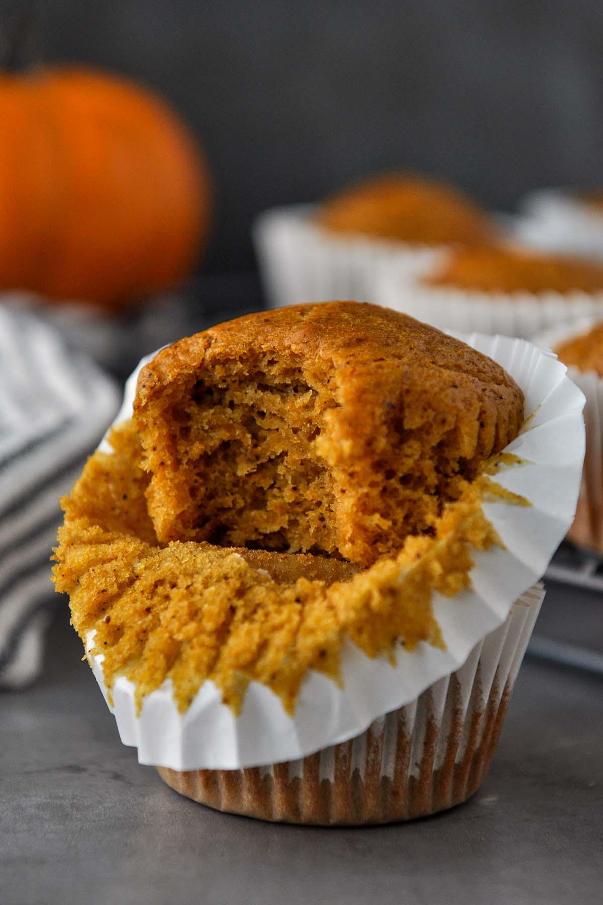 A muffins with a big bite out of it with a pumpkin in the background.