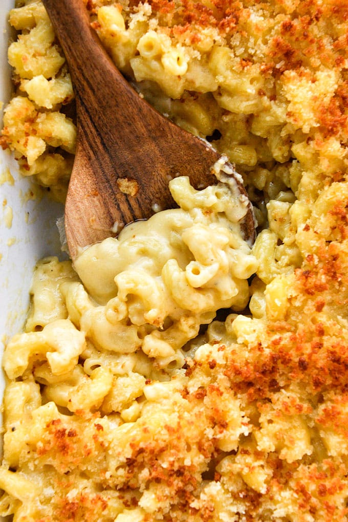 An above view of a spoon in creamy macaroni and cheese with a browned crumb topping.