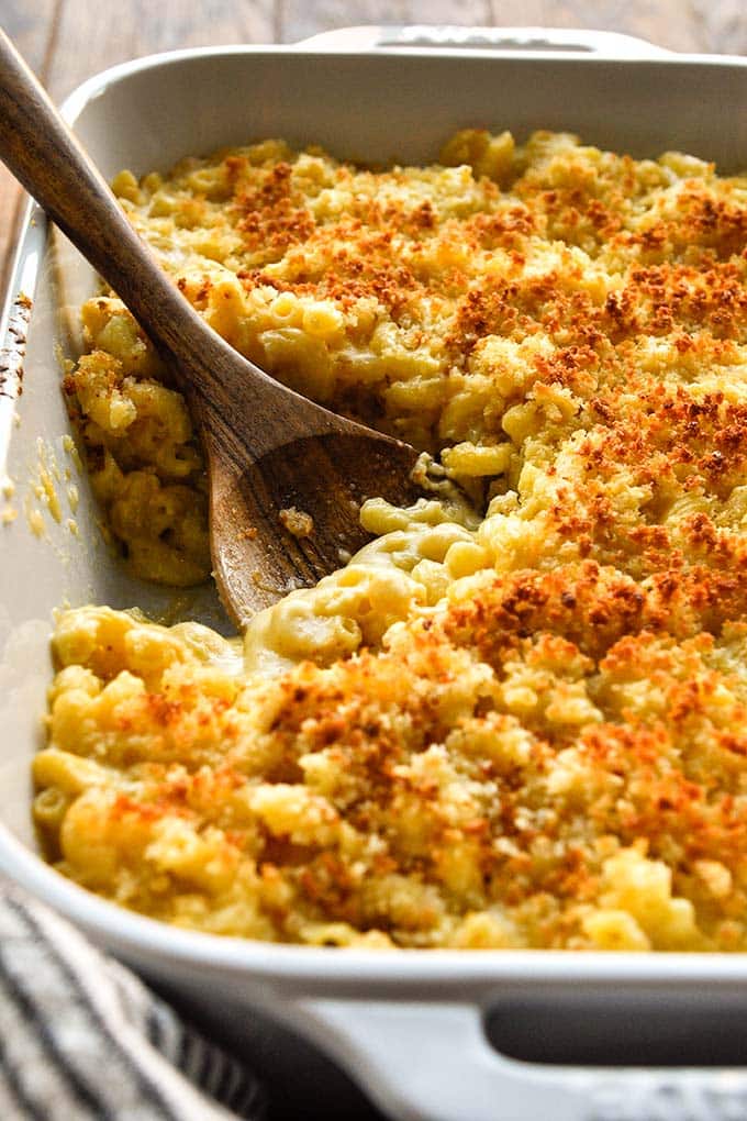 A baking dish full of just out of the oven mac and cheese with a wooden spoon.