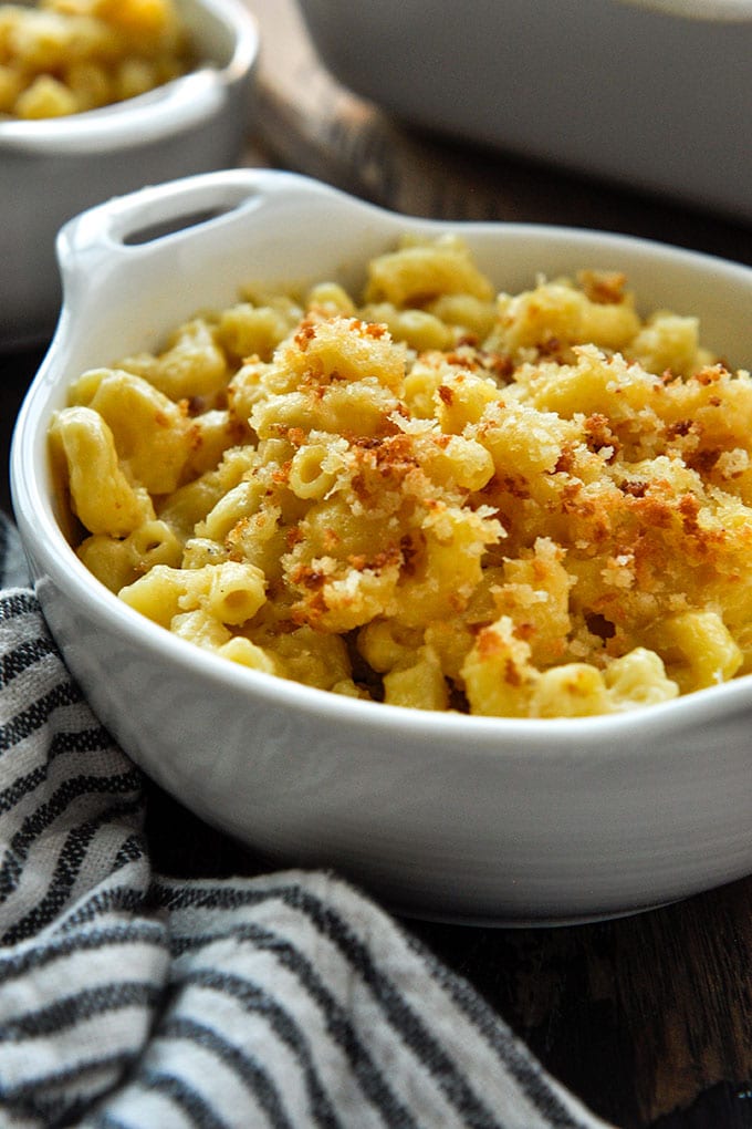 A bowl of homemade macaroni and cheese with a crunchy topping and a white and blue striped towel.
