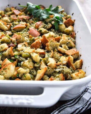 A baking pan full of stuffing with a sprig of parsley sprig and a black and white towel.