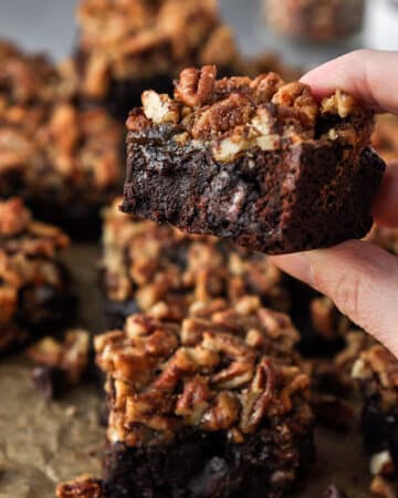 A gooey pecan pie brownie being held up with other brownies in the background.