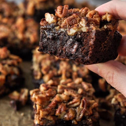 A gooey pecan pie brownie being held up with other brownies in the background.