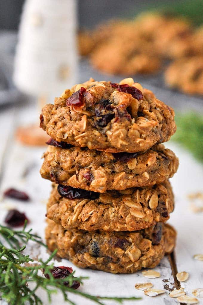 A stack of cranberry walnut oatmeal cookies with a cooling rack of cookies and a small white Christmas tree in the background.