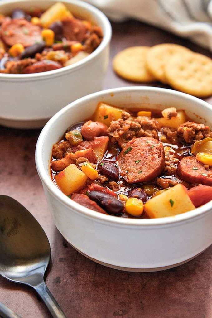 A bowl of cowboy stew with a spoon and some crackers.
