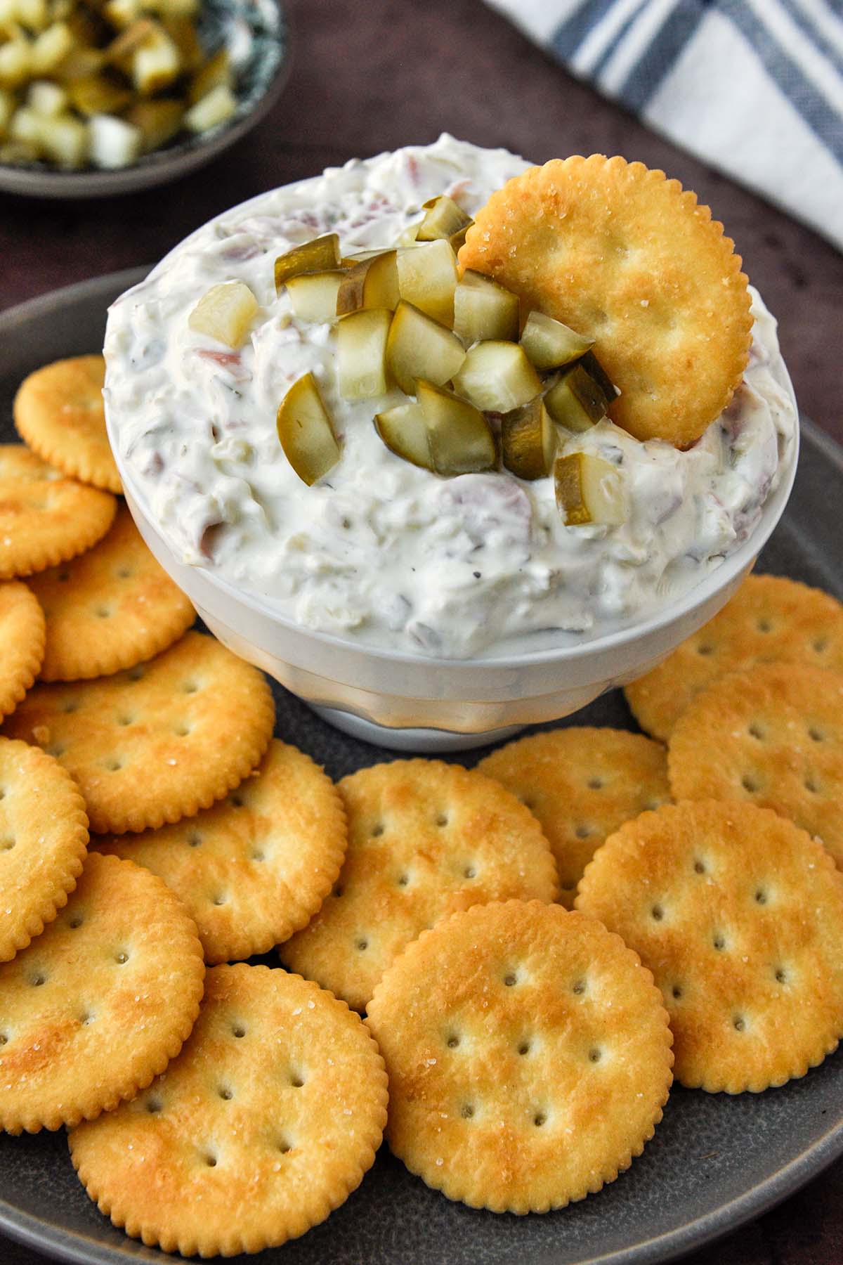 A bowl of pickle wrap dip with a cracker on a tray of crackers.
